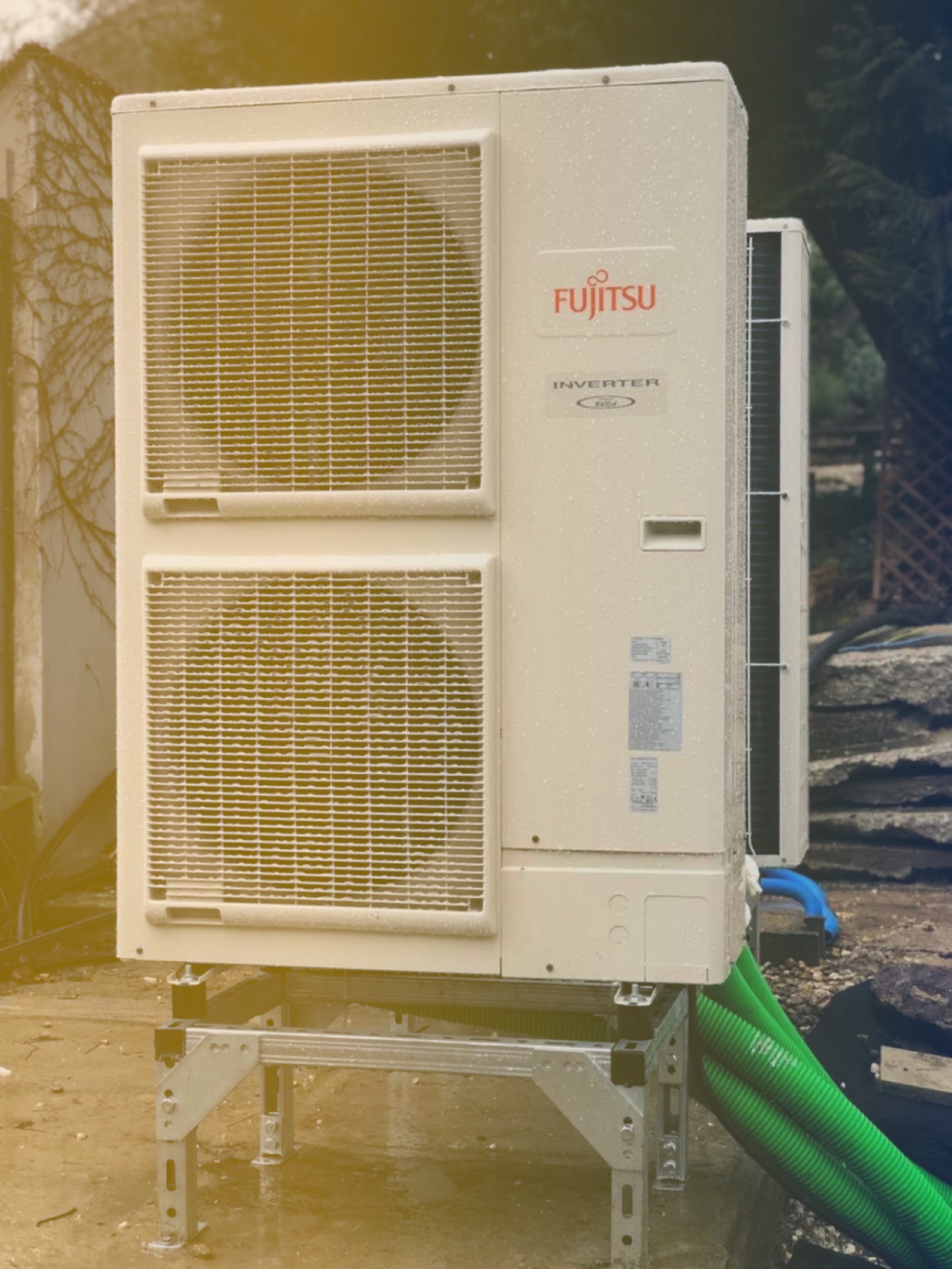 Fujitsu inverteres hőszivattyú kültéri egysége állványon, egy családi ház mellett
